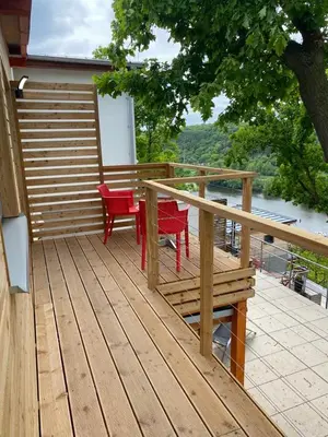 a wooden deck with red chairs and a table at Apartmán - E - Vyhlídka nad řekou in Zdiby