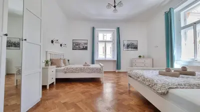 a white bedroom with two beds and wooden floors at Finnem Rentals Tyršova in Prague