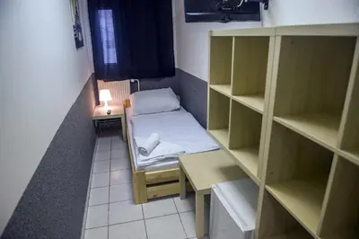 a small room with a bed and a desk and shelves at Hostel Seven in Prague