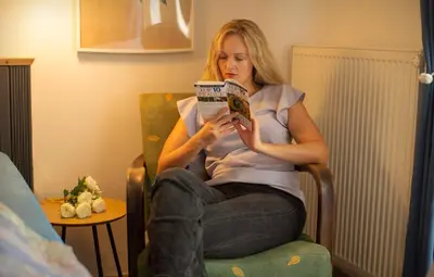 a woman sitting in a chair reading a magazine at Triple King Size Balcony Suite in Prague