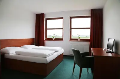 a bedroom with a bed and a desk and two windows at Sporthotel Hostivice in Hostivice
