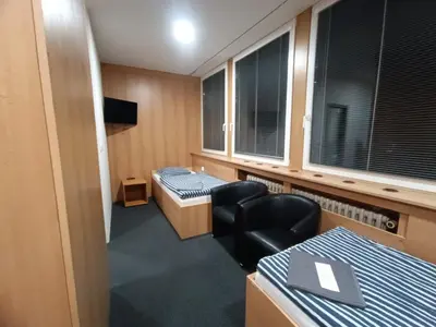 a room with two beds and a chair and windows at Hotel a ubytovna Zimní stadion Slaný in Slaný