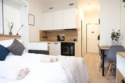 a bedroom with a white bed and a kitchen at Rentero MyMozart Apartments Prague in Prague