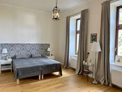 a bedroom with a bed and a table and windows at Zámek Jenišovice in Býkev