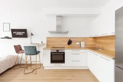 a kitchen with white cabinets and a sink and a bed at Prague Days - Studio with Balcony in quiet and trendy Holešovice in Prague