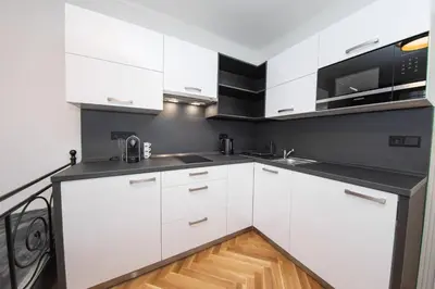 a white kitchen with white cabinets and a wooden floor at Nekazanka studio apartment in Prague