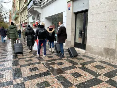a group of people walking down a sidewalk with luggage at TDC31, boo in Prague