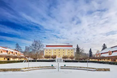 a large yellow building with a red roof in the snow at Dvůr Pecínov in Benešov