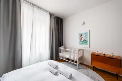 a white bedroom with a crib and a window at Gallery Apartment in Prague