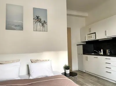a white bedroom with a bed and a kitchen at Parkside Studio in Vinohrady in Prague