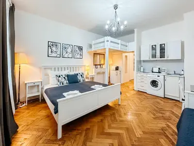 a bedroom with a white bed and a kitchen at ELSO center apartment in Prague