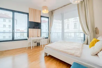 a bedroom with a bed and a desk and large windows at New-built Golden Luxury Studio with Balcony in Prague