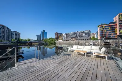 a wooden deck with a couch on a dock next to the water at Hausboat Holešovice in Prague