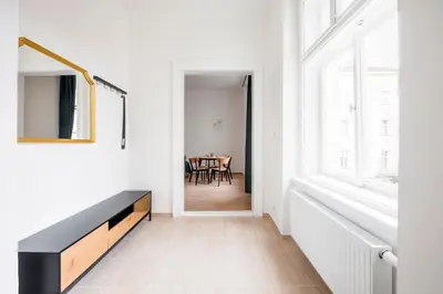 a white hallway with a black bench and a dining room at City center premium apartment in Prague
