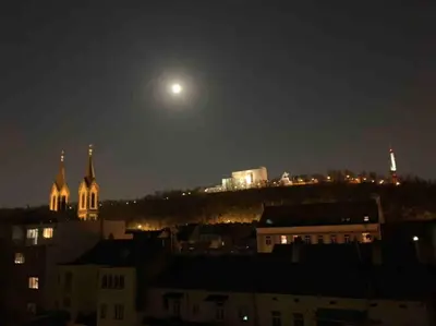 a view of a city at night with the moon at Romantic Terrace Studio in Karlín in Prague