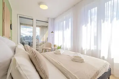 a white bedroom with a bed and a large window at Bright 2BR - 8th floor, Balcony, Free Parking - by Gravity Prague in Prague