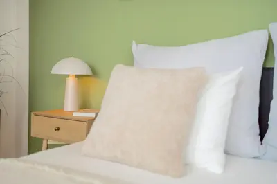 a bed with white pillows and a table with a lamp at Bright 2BR - 7th floor, Balcony, Free Parking by Gravity Prague in Prague