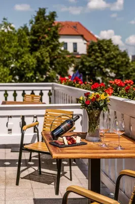 a wooden table with a bottle of wine and flowers on a balcony at Prague Hotel Carl Inn restaurant & Free Parking in Prague