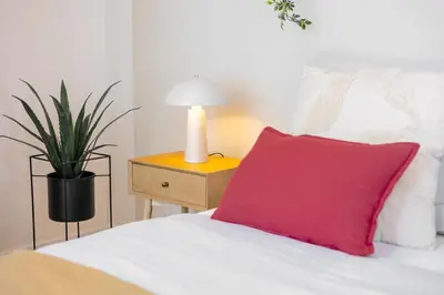 a bed with a red pillow and a table with a plant at Bright 2BR - 5th floor, Balcony, Free Parking by Gravity Prague in Prague