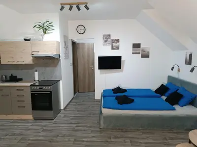 a bedroom with a blue bed and a kitchen at Apartmán Pod Hrází Chráštany in Benešov