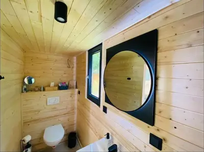 a bathroom with a circular mirror in a wooden wall at Glamping paradise with wellness in Dolní Břežany