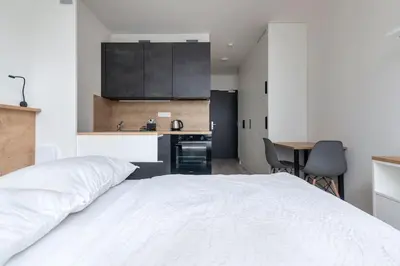 a bedroom with a white bed and a kitchen at Central Tiny Flat, 1GB WiFi, SMART TV, Air Condition in Prague