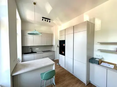 a kitchen with white cabinets and a green chair at Onefam Arbes in Prague