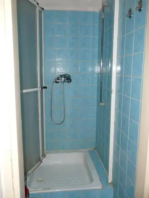a blue tiled bathroom with a shower with a glass door at Apartment Trojska in Prague