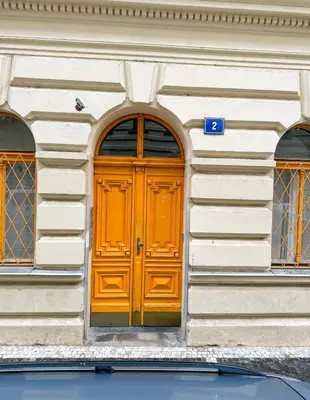 an orange door on a white building with two windows at Vantisch Old Town Apartment in Prague