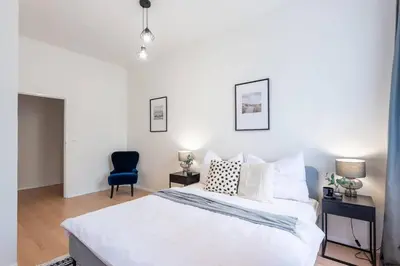 a bedroom with a white bed and a blue chair at Urban 2BR Haven with Sofa Bed in Central Prague in Prague