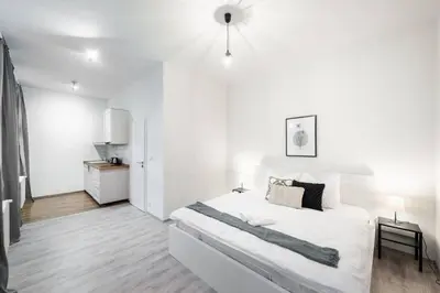 a white bedroom with a large bed and a kitchen at Tranquil Prague Studio Gem in Prague