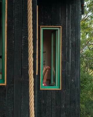 a window of a black building with a woman in a mirror at Veritas Beyond Glamping in Hošťka