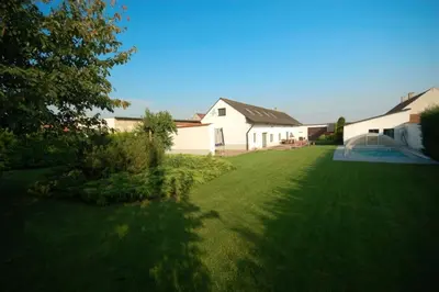 a large yard with a white house and a tree at Příjemné místo pro odpočinek s bazeném in Radovesice