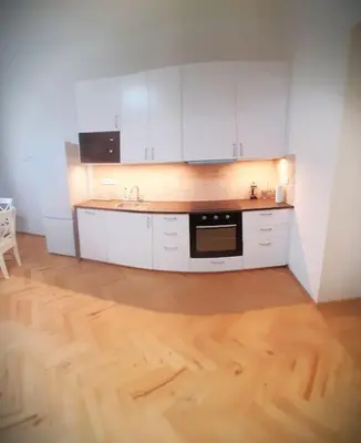 a kitchen with white cabinets and a wooden floor at Arbes apartman in Prague