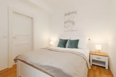 a white bedroom with a white bed with blue pillows at Louvre - Cozy City Center Apartment with Balcony in Prague
