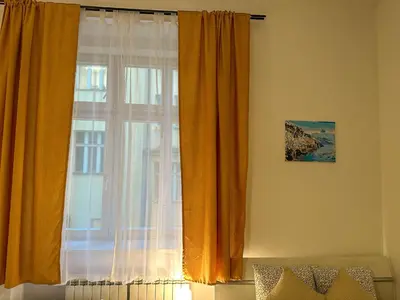 a window with orange curtains next to a bed at Cozy Apartment by Wenceslas Square and Main Train Station in Prague