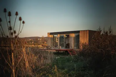 a small house in a field with the sun setting at Glamping Jezeroooo Lipence in Prague