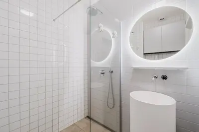 a white tiled bathroom with a shower and a mirror at Blueground Vinohrady close to Namesti Miru PRG-2 in Prague