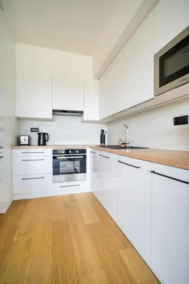 a white kitchen with white cabinets and a wooden floor at Czech TESLA apartment by Rentez in Prague