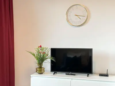 a tv on a white cabinet with a clock and flowers at REAL Living by REFA Balcony Retreat 75 in Prague
