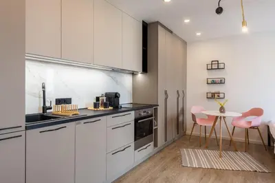 a kitchen with white cabinets and a table with pink chairs at Sunset View Apartment in Prague