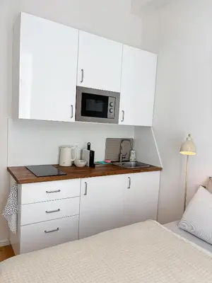 a white kitchen with a microwave and a bed at Museum Park Apartment in Prague
