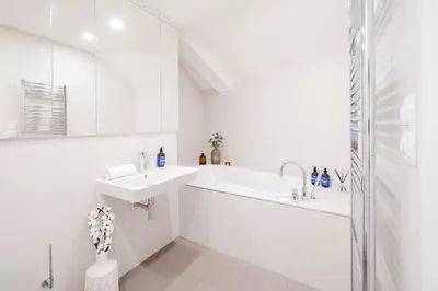 a white bathroom with a tub and a sink at Prague Days - Two-Bedroom Maisonette with AC and Terrace with Grill in Vinohrady in Prague