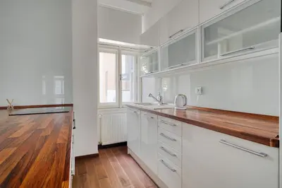 a kitchen with white cabinets and a wooden floor at Botanical Escape Apartment in Prague