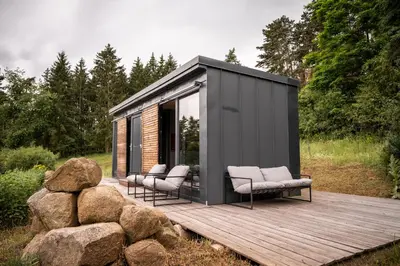 a black shed with three chairs on a wooden deck at Tiny House Sedla in Velká