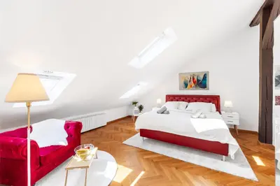 a white bedroom with a red bed and a red chair at Cozy Luxe Home at the Heart of Old Prague Centre in Prague