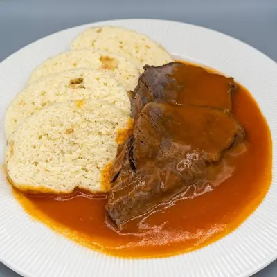 a plate with a piece of meat and bread with sauce at Hotel Junior Poděbrady in Poděbrady