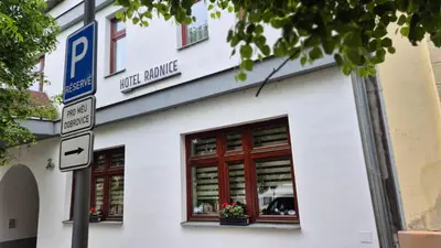 a white building with red windows and a parking sign at Hotel Radnice Dobrovice in Dobrovice
