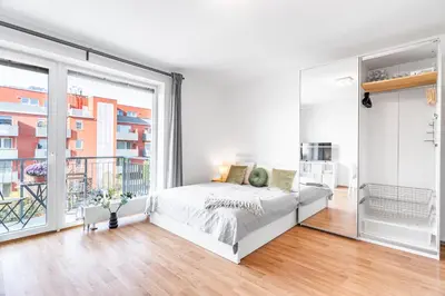 a white bedroom with a bed and a balcony at Airport Apartman Víšek in Chýně