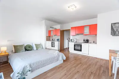 a bedroom with a bed and a kitchen with red cabinets at Airport Apartman Víšek in Chýně